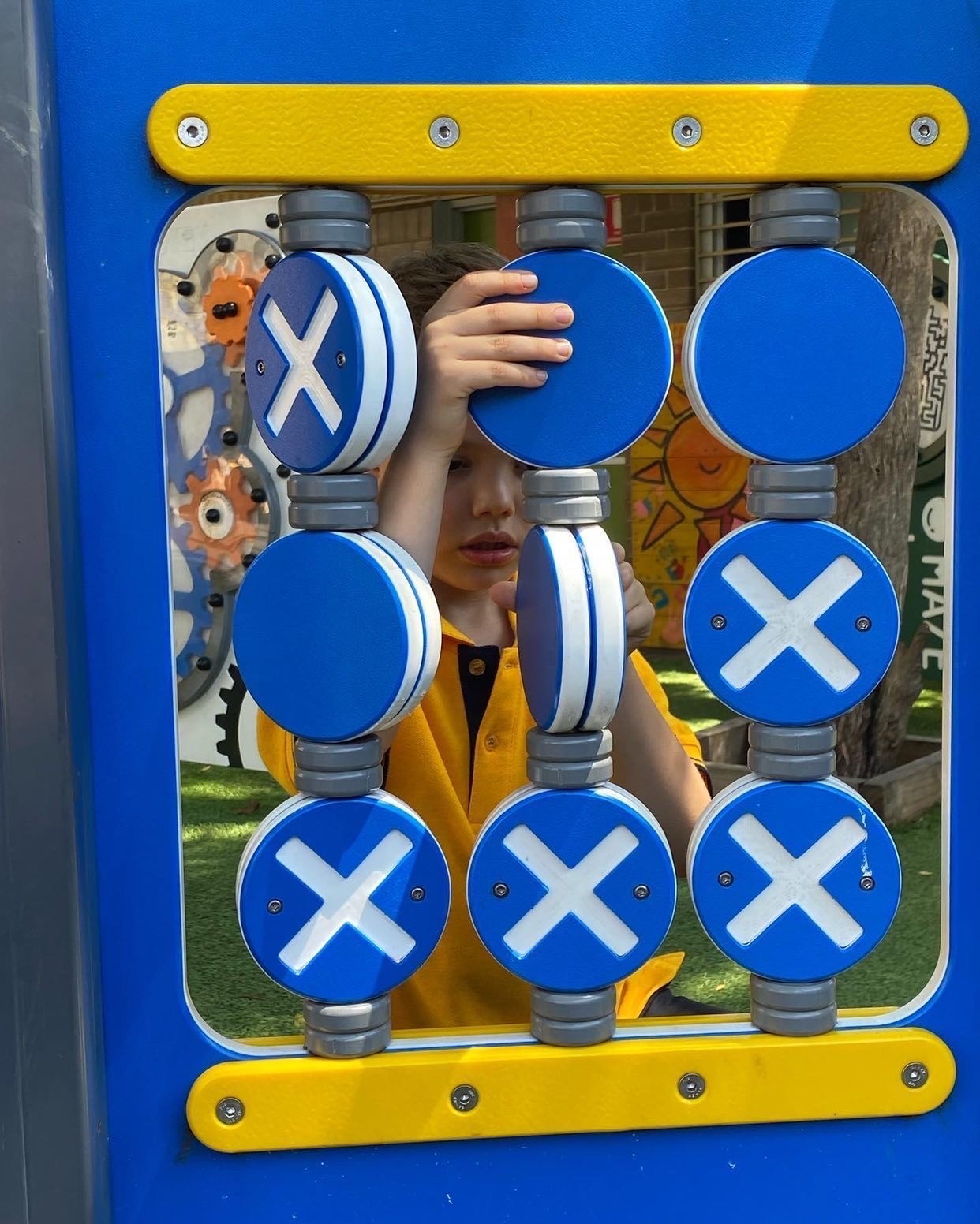 Young school boy playing with "X&O's - Noughts & Crosses" Sensory Panel in an outdoor playground